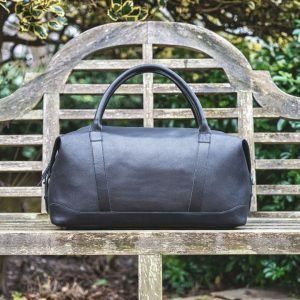 a black leather holdall sitting on a wood bench