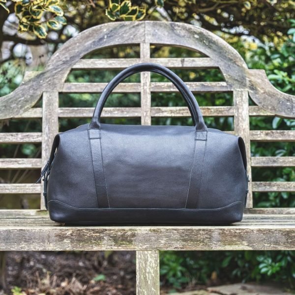 a black leather holdall sitting on a wood bench