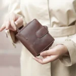 brown leather bifold purse with a zip-around closure and a front snap button strap.