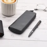 Black leather zipped pen case on desk beside coffee cup, pen, and glasses