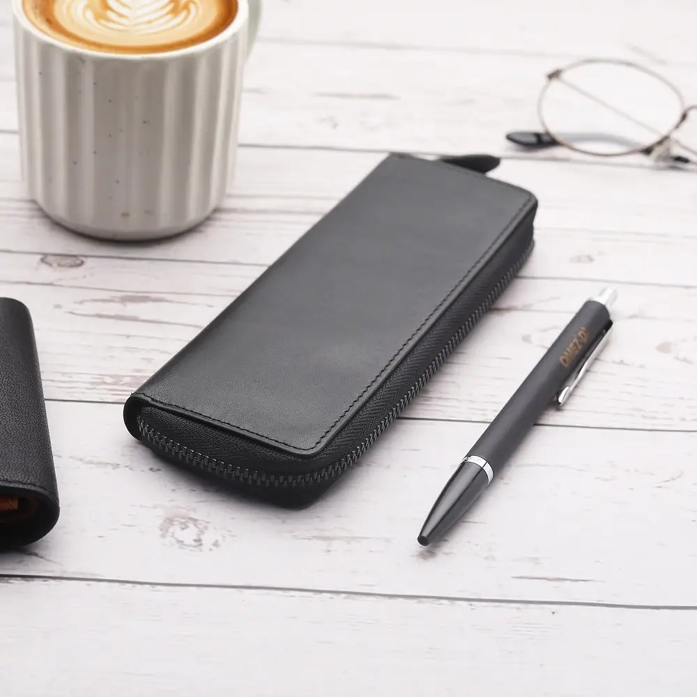 Black leather zipped pen case on desk beside coffee cup, pen, and glasses