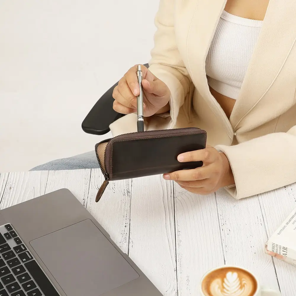 Brown leather zipped pen case on an office desk beside a coffee cup and laptop