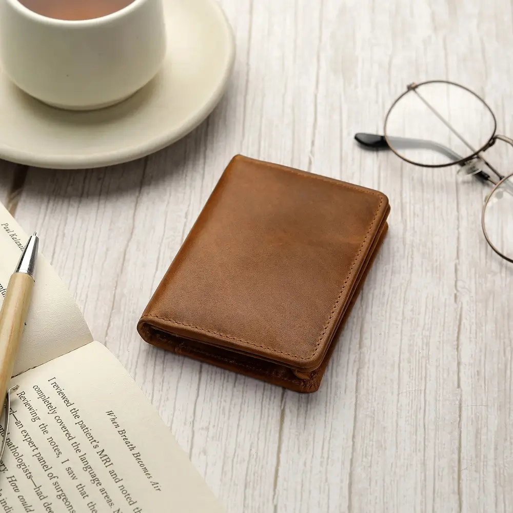 Tan leather Mayfair 2511 credit cardholder placed on a wooden café table beside a coffee cup and glasses.